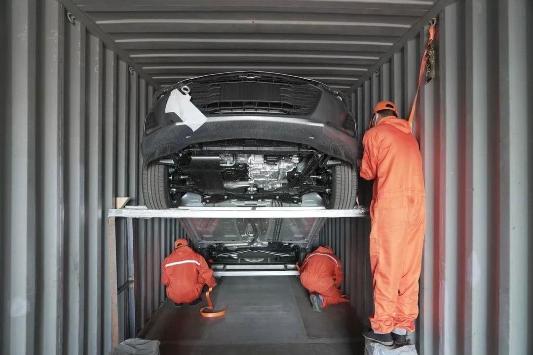 Workers securing a car inside a container before shipping